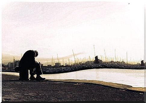 A sad old man sits alone in front of a lake.